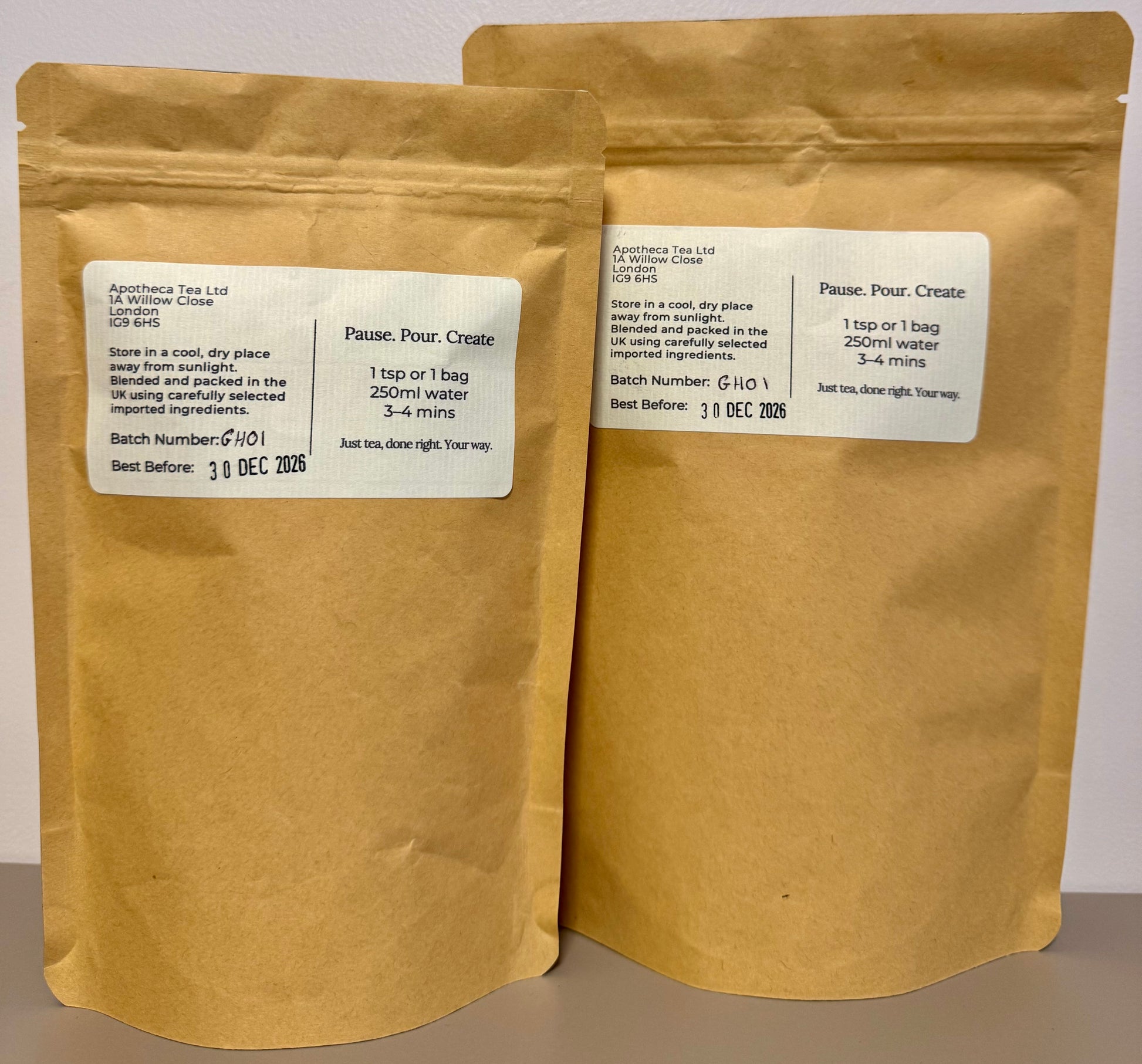 Two brown paper tea bags with labels on a neutral background