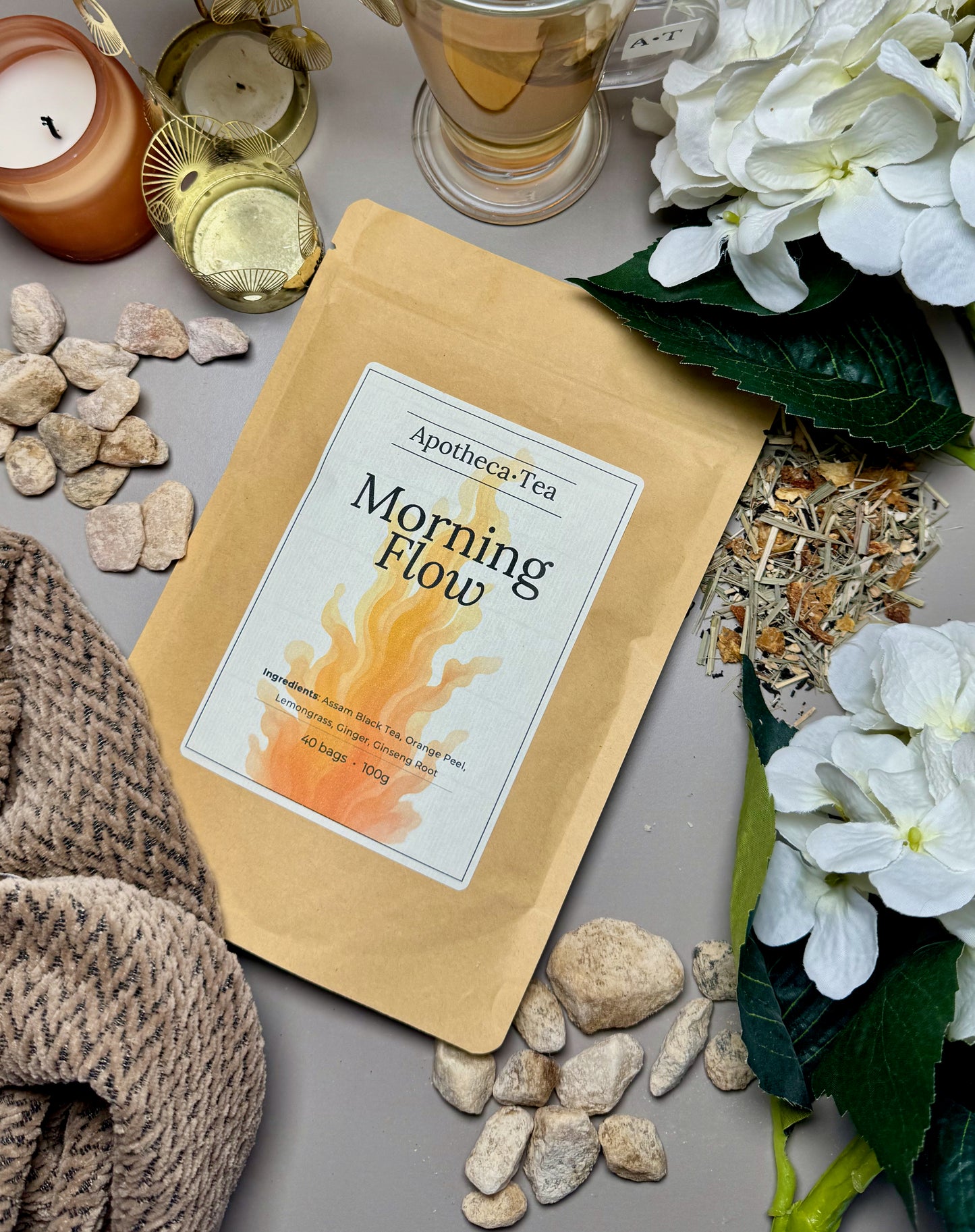 Apotheca-Tea 'Morning Flow' package on a surface with candles, flowers, and stones.