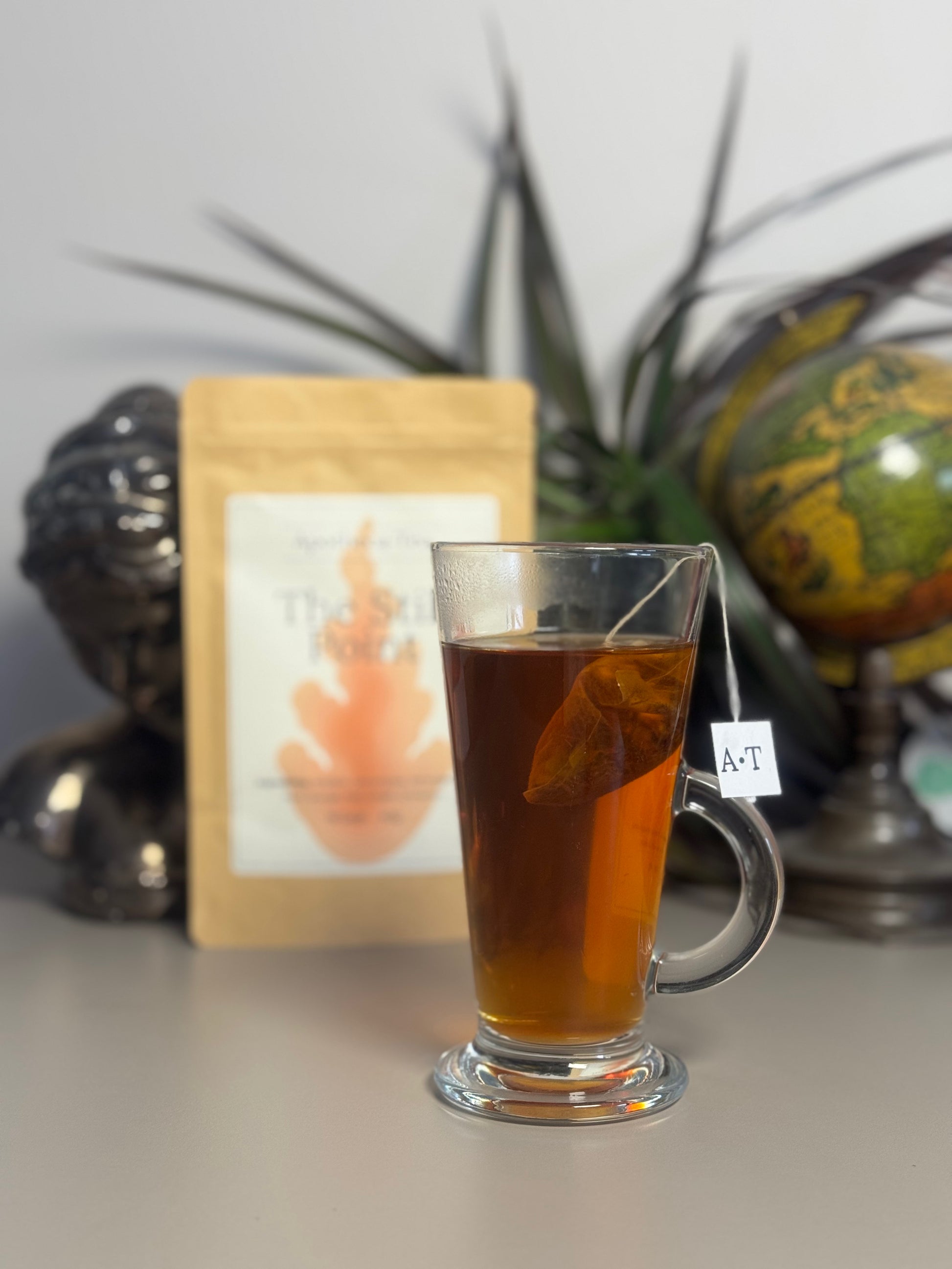 Clear glass mug filled with iced tea on a reflective surface with decorative items in the background.