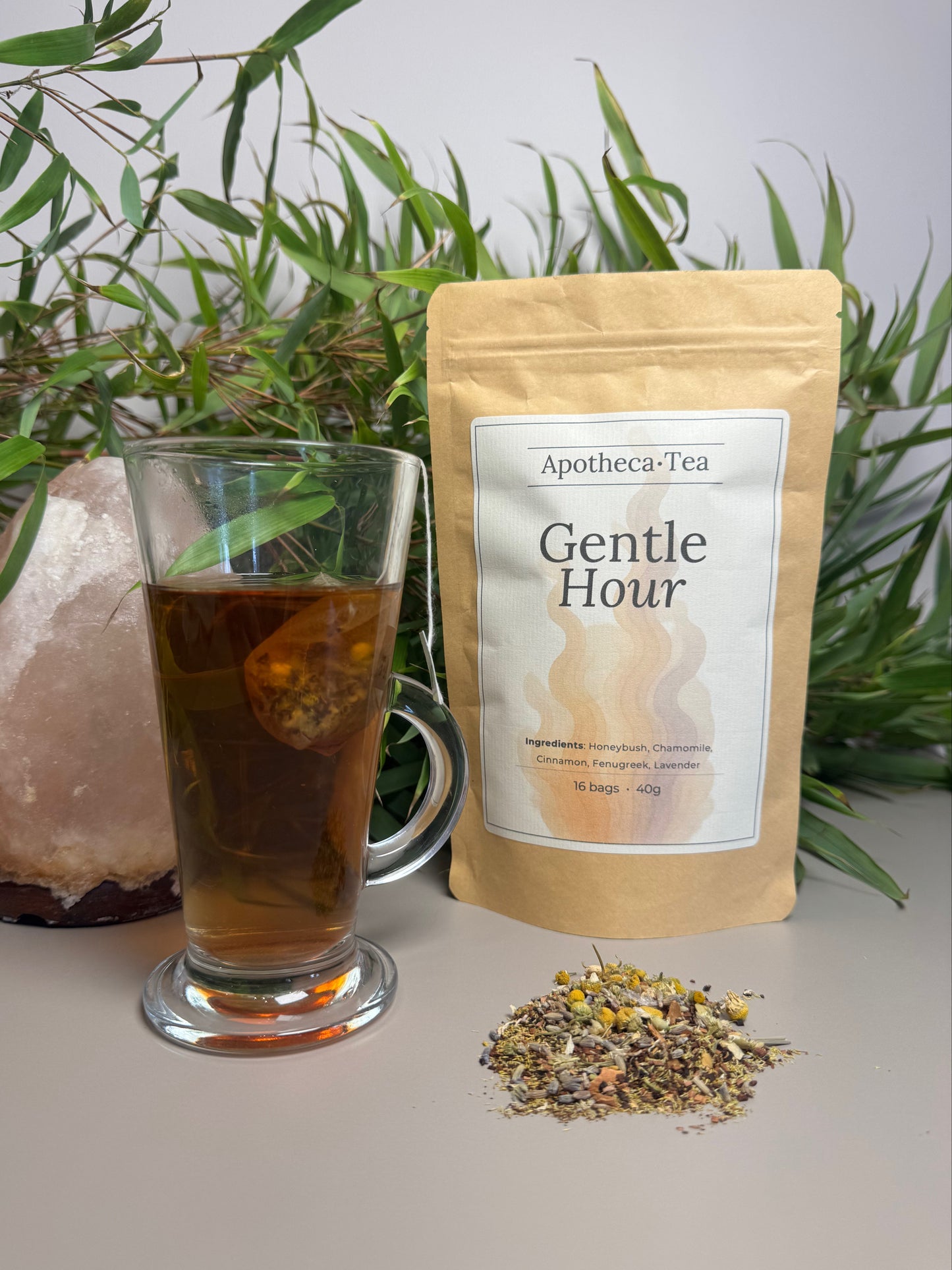 Apotheca-Tea Gentle Hour package with a glass of tea and tea leaves on a light surface with plants in the background.